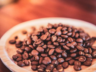 Orta pişmiş kahve çekirdekleri en üstteki ahşap tabakta kahverengi bir ahşap masaya yerleştirilir. Kahve ile ilgili çalışma geçmişi için resim fikri.