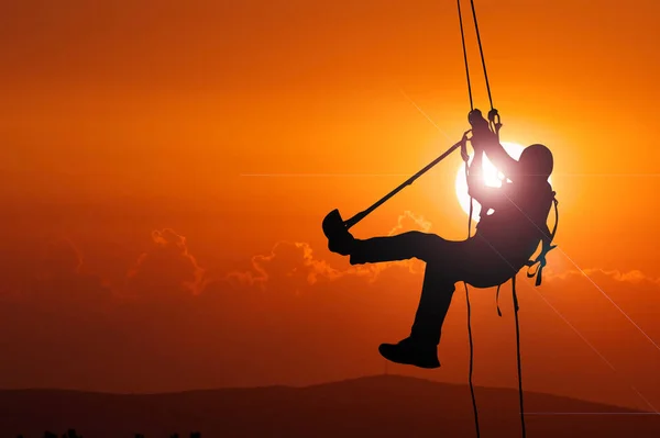 Silhouette of an adventurer climbing a rope on a high cliff in the evening. with clipping path
