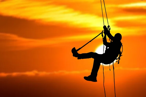 Silhouette of an adventurer climbing a rope on a high cliff in the evening. with clipping path