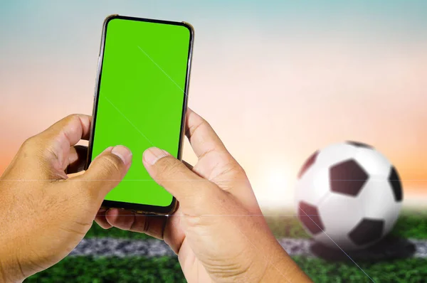 green blank screen mobile phone in man\'s hand with football background