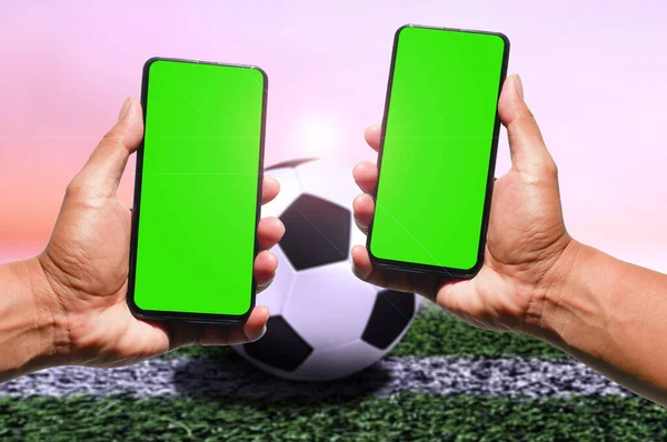 green blank screen mobile phone in man\'s hand with football background