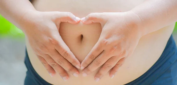 a pregnant woman with a heart-shaped hand placed on her stomach