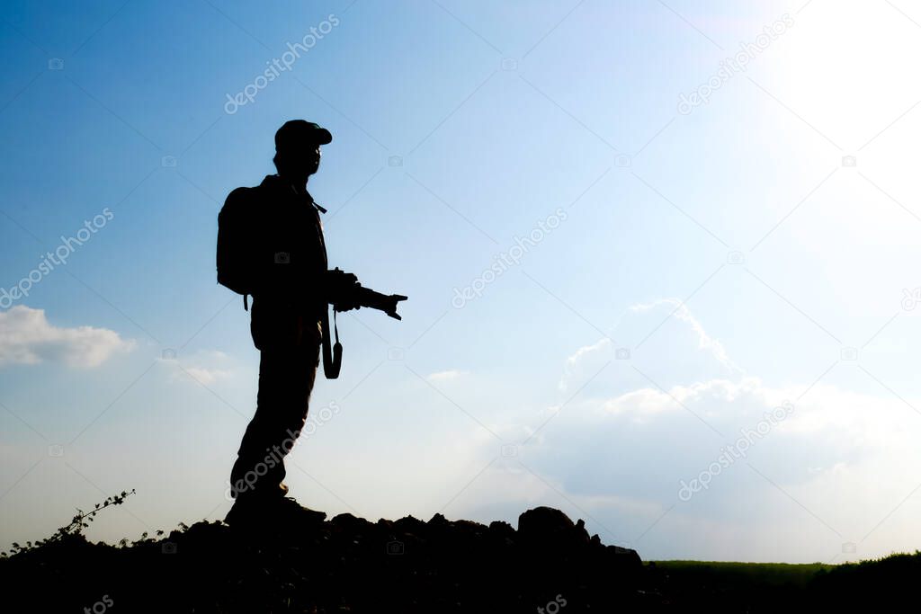 Silhouette of a professional landscape travel photographer holding a camera on a mountain.