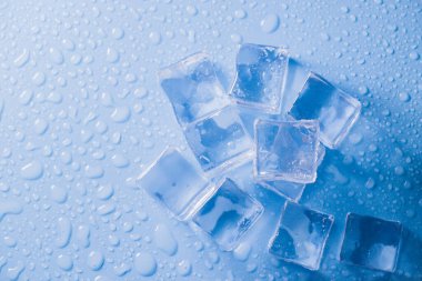 Buz küplerinin makro görüntüsü ve mavi arkaplanda boş boşluğu kopyalayan su damlaları. Mavi arkaplana dağılmış su damlaları olan buz küpleri