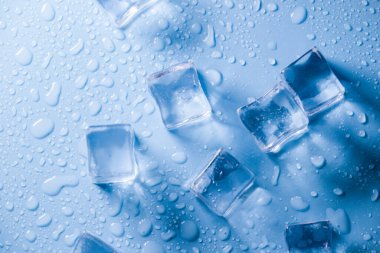 Buz küplerinin makro görüntüsü ve mavi arkaplanda boş boşluğu kopyalayan su damlaları. Mavi arkaplana dağılmış su damlaları olan buz küpleri