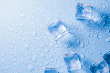 Buz küplerinin makro görüntüsü ve mavi arkaplanda boş boşluğu kopyalayan su damlaları. Mavi arkaplana dağılmış su damlaları olan buz küpleri