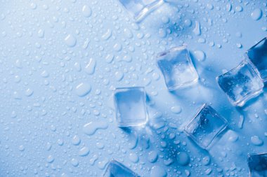 Buz küplerinin makro görüntüsü ve mavi arkaplanda boş boşluğu kopyalayan su damlaları. Mavi arkaplana dağılmış su damlaları olan buz küpleri