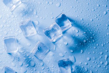 Buz küplerinin makro görüntüsü ve mavi arkaplanda boş boşluğu kopyalayan su damlaları. Mavi arkaplana dağılmış su damlaları olan buz küpleri