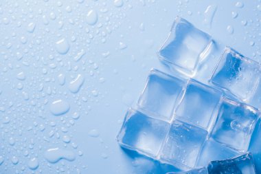 Buz küplerinin makro görüntüsü ve mavi arkaplanda boş boşluğu kopyalayan su damlaları. Mavi arkaplana dağılmış su damlaları olan buz küpleri