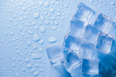 Buz küplerinin makro görüntüsü ve mavi arkaplanda boş boşluğu kopyalayan su damlaları. Mavi arkaplana dağılmış su damlaları olan buz küpleri