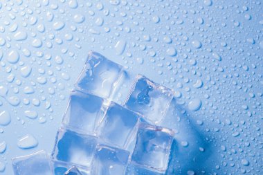 Buz küplerinin makro görüntüsü ve mavi arkaplanda boş boşluğu kopyalayan su damlaları. Mavi arkaplana dağılmış su damlaları olan buz küpleri