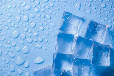 Buz küplerinin makro görüntüsü ve mavi arkaplanda boş boşluğu kopyalayan su damlaları. Mavi arkaplana dağılmış su damlaları olan buz küpleri