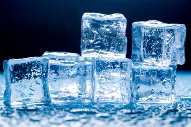 Buz küplerinin makro görüntüsü ve mavi arkaplanda boş boşluğu kopyalayan su damlaları. Mavi arkaplana dağılmış su damlaları olan buz küpleri