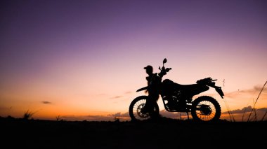 Gün batımında motosikletli bir adamın silueti.