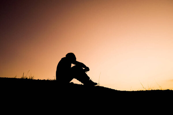 Силуэт человека, сидящего в отчаянии в одиночестве вечером.