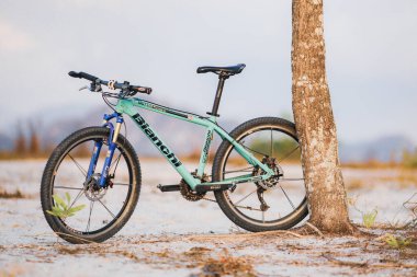 23 Temmuz 2021 'de, Surat Thani, Tayland' da, mutlu bir bisikletçi ve bir dağ bisikleti off-road yolunda bir ağaca park etmiş..