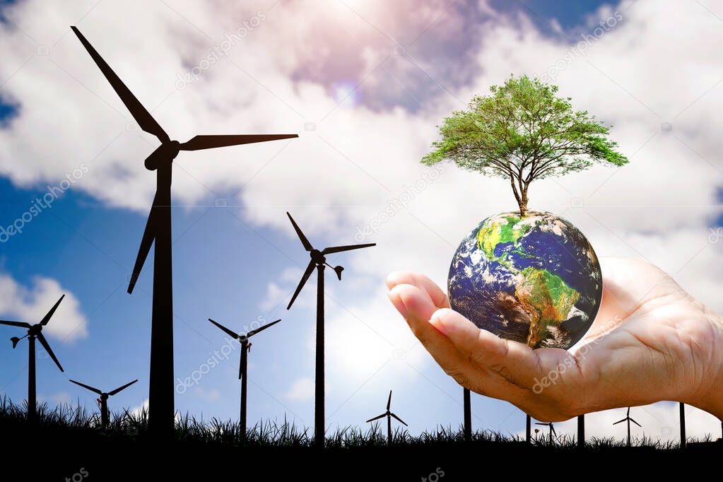 Clean energy concept to reduce global warming. hand holding a globe with a tree The background is a wind turbine generating electricity.