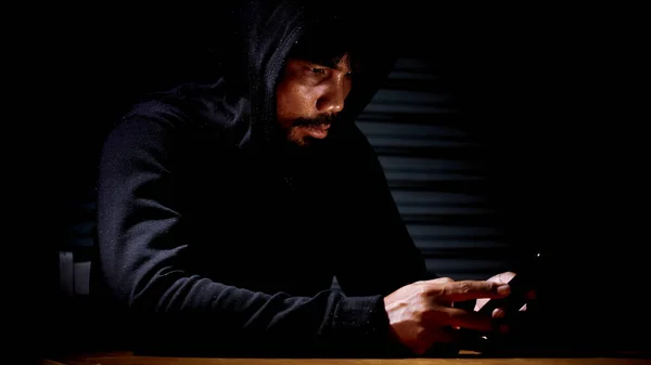 Mysterious man in hoodie on dark background. Dangerous criminal. Silhouette of man in the hood, dark mysterious man hoodie, murderer, hacker, anonymus on the black background with free space