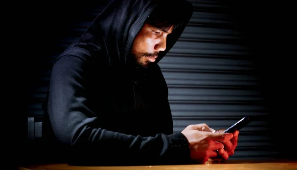 Mysterious man in hoodie on dark background. Dangerous criminal. Silhouette of man in the hood, dark mysterious man hoodie, murderer, hacker, anonymus on the black background with free space