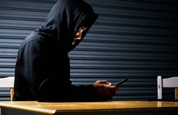 Mysterious man in hoodie on dark background. Dangerous criminal. Silhouette of man in the hood, dark mysterious man hoodie, murderer, hacker, anonymus on the black background with free space