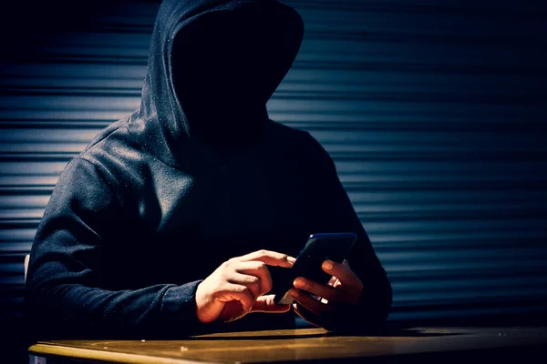 Mysterious man in hoodie on dark background. Dangerous criminal. Silhouette of man in the hood, dark mysterious man hoodie, murderer, hacker, anonymus on the black background with free space