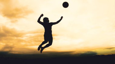 Bir voleybol oyuncusunun silueti dağda pratik yapıyor ve akşam çok güzel bir manzara sunuyor.