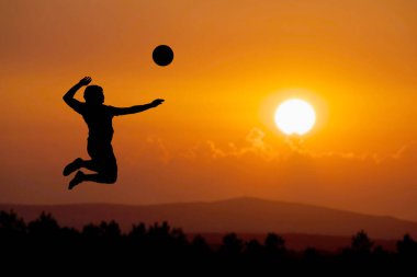 Bir plaj voleybolcusunun silueti atlayıp voleybol topuna vuruyor..