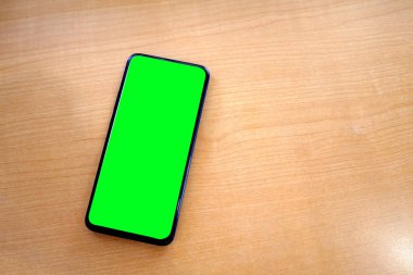 Kahverengi ahşap masadaki cep telefonu içerik kopyalama alanı için kırpma yolu olan boş ekran