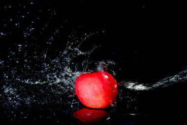Sudaki kırmızı elmalar siyah arkaplanda sıçrıyor. Elma suyu siyah arkaplanda sıçrar