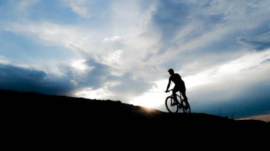 Bisikletçi silueti. Arka planda gökyüzü olan kumlu bir sahilde bisiklet turu.