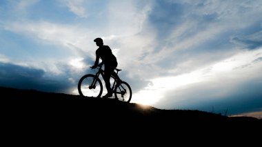 Bisikletçi silueti. Arka planda gökyüzü olan kumlu bir sahilde bisiklet turu.