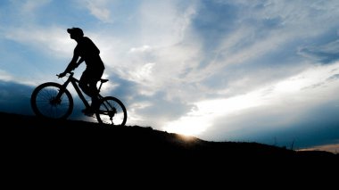 Bisikletçi silueti. Arka planda gökyüzü olan kumlu bir sahilde bisiklet turu.