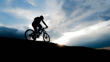 Bisikletçi silueti. Arka planda gökyüzü olan kumlu bir sahilde bisiklet turu.