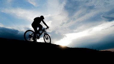 Bisikletçi silueti. Arka planda gökyüzü olan kumlu bir sahilde bisiklet turu.