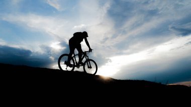 Bisikletçi silueti. Arka planda gökyüzü olan kumlu bir sahilde bisiklet turu.