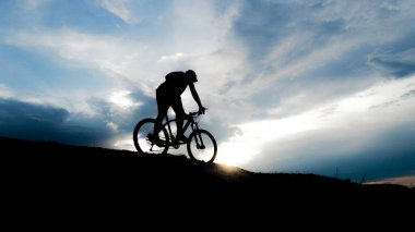 Bisikletçi silueti. Arka planda gökyüzü olan kumlu bir sahilde bisiklet turu.