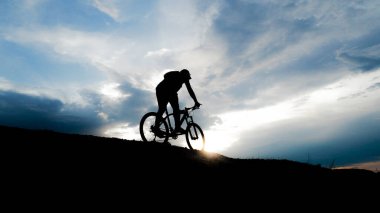 Bisikletçi silueti. Arka planda gökyüzü olan kumlu bir sahilde bisiklet turu.