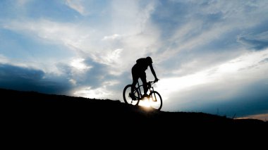 Bisikletçi silueti. Arka planda gökyüzü olan kumlu bir sahilde bisiklet turu.