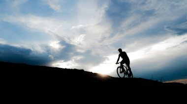 Bisikletçi silueti. Arka planda gökyüzü olan kumlu bir sahilde bisiklet turu.