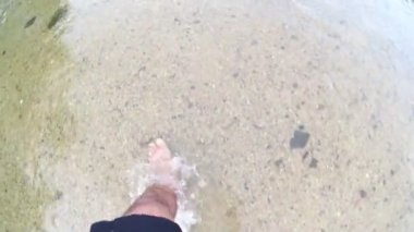  man's bare feet walking  in water at a beach 