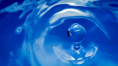 Su damlası mavi renklidir. Yuvarlak su damlası. Bardakta su damlası. Damlalar, sıçramalar, spreyler, sudan soyut şekiller. Su sıçrattı. Yağmur damlaları suyun pürüzsüz yüzeyine düşüyor