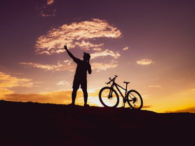 Günbatımı arka planında dağ bisikleti olan bir adamın silueti.