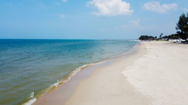 Sakin dalgalar, kumlu kıyılar ve berrak mavi gökyüzü ile huzurlu tropik plaj sahnesi seyahat ve rahatlama temaları için mükemmel..