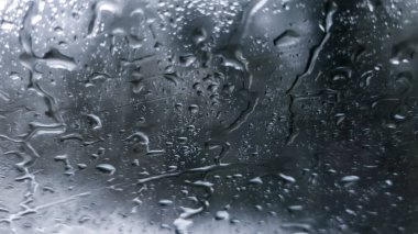 Camdan pencereye konan yağmur damlaları karamsar gri gökyüzüne karşı soyut bir desen oluşturuyor..