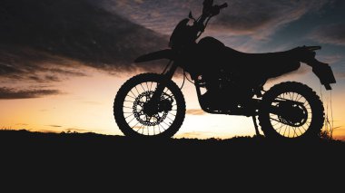 Renkli bir günbatımı gökyüzüne karşı, macera ve özgürlüğün özünü yakalayan çarpıcı bir motosiklet silueti..