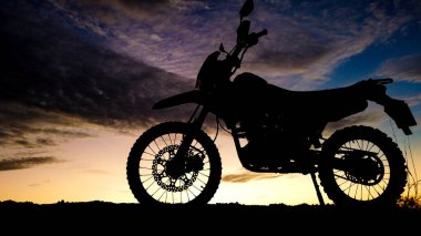 * * Engebeli bir off-road motosikletinin silueti rengarenk bir günbatımı gökyüzüne karşı, macera ve özgürlüğü vurguluyor.