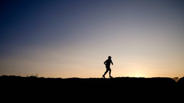 Yanlız bir koşucu, canlı bir günbatımı gökyüzüne karşı, yalnızlığın ve kararlılığın özünü yakalıyor..