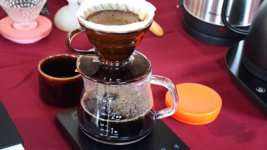 Dijital ölçekte cam damlatıcı ve sürahi ile kahve üzerine dökülen bardağın yakın plan görüntüsü, demleme sürecini gösteriyor.