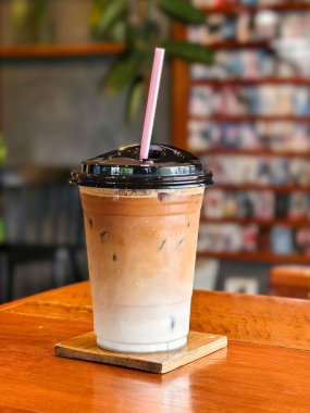 Sade bir fincanda servis edilen pipetle nefis bir buzlu kahve, rahat bir kafe ortamında ahşap bir masaya konur..