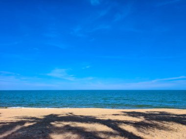 Altın kum, mavi okyanus ve berrak gökyüzü ile sakin plaj sahnesi, rahatlama ve seyahat için mükemmel..
